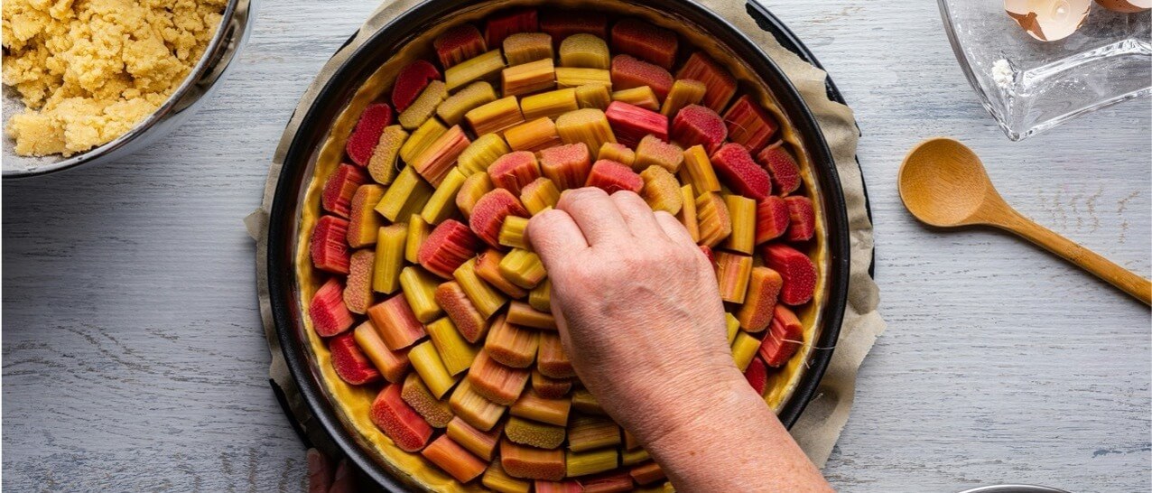 Person placing sliced rhubarb into a pie case, creating a circular pattern.